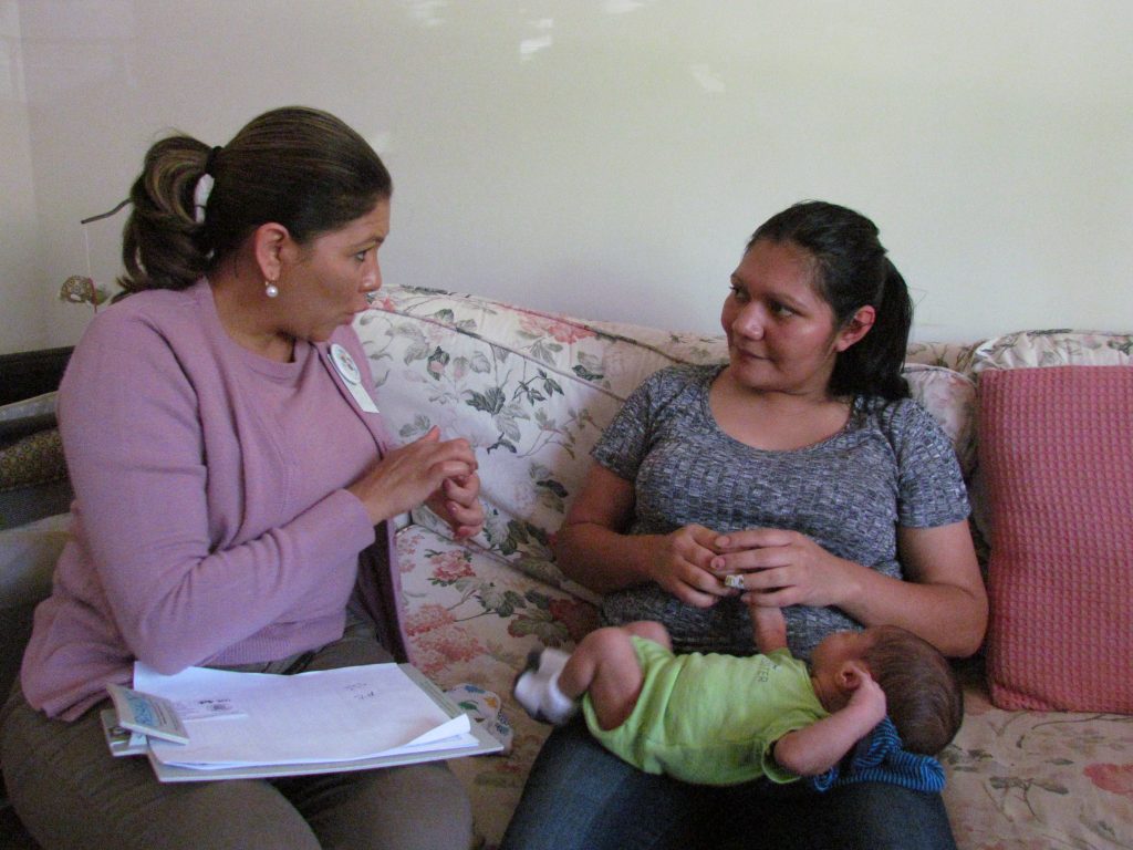 Woman talking to a mother with infant on her lap.