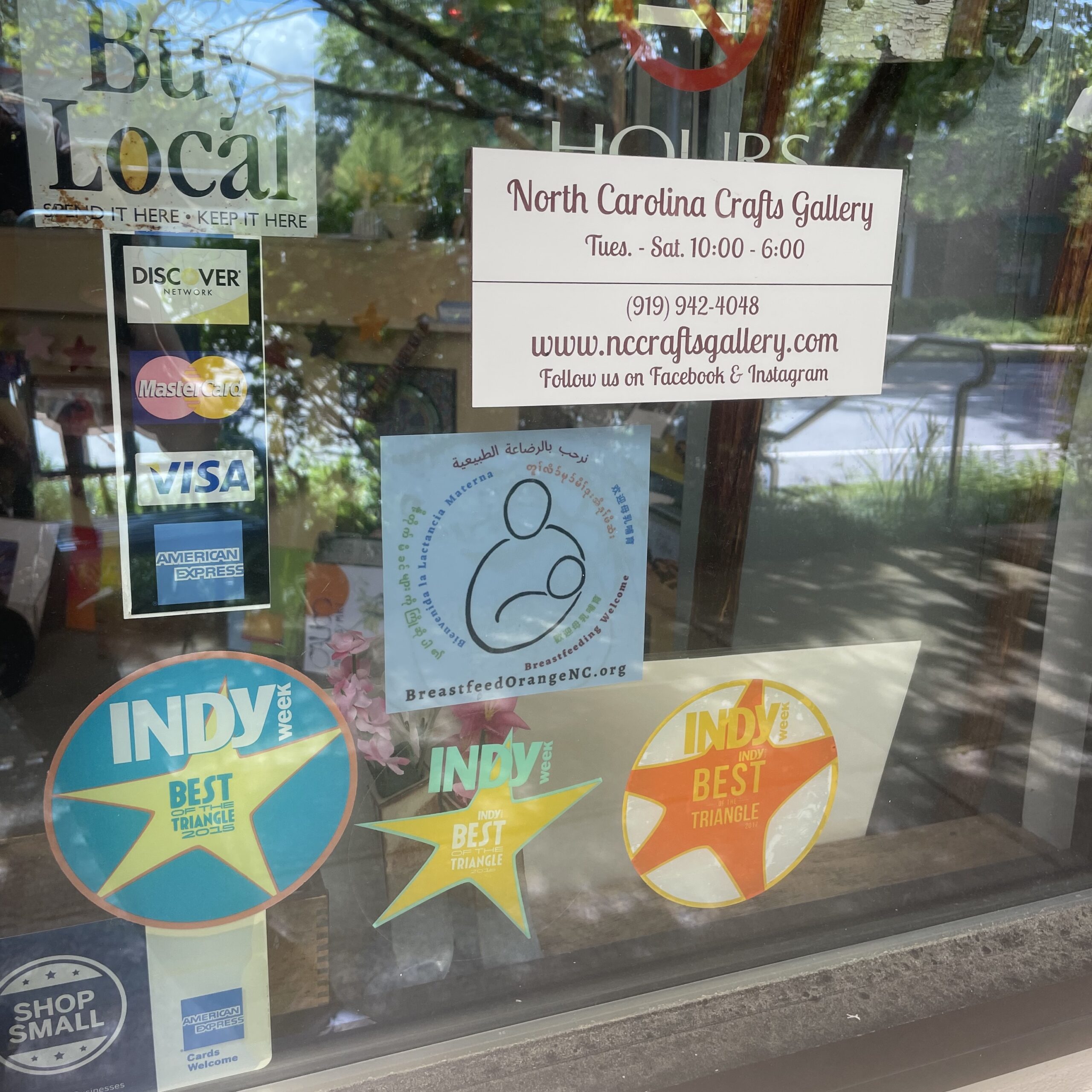 Window of NC Craft Gallery with Breastfeed Orange NC logo and other window clings
