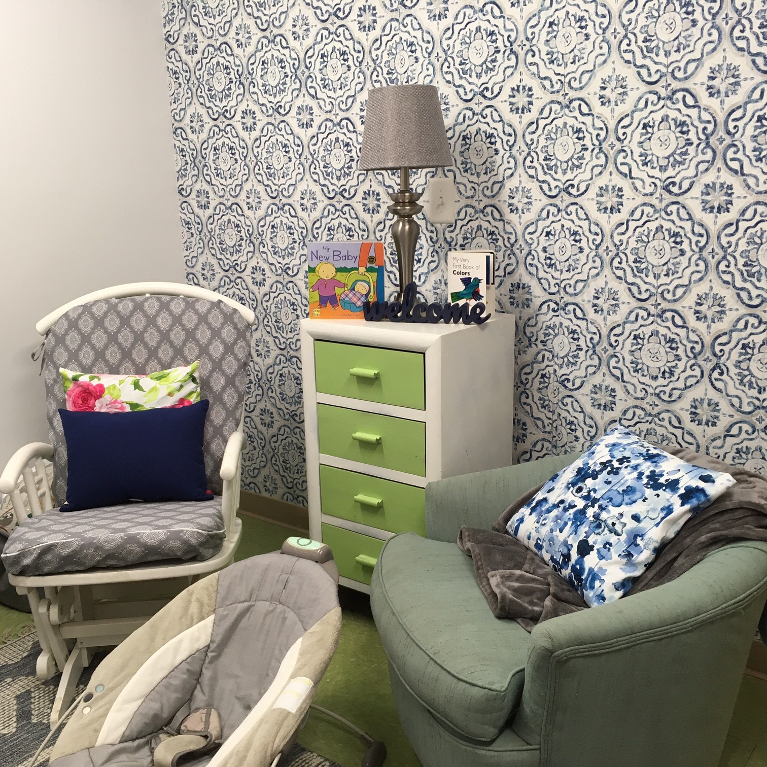Image of a lactation space with a cushioned chair, a rocking chair, and a lamp on a small dresser.