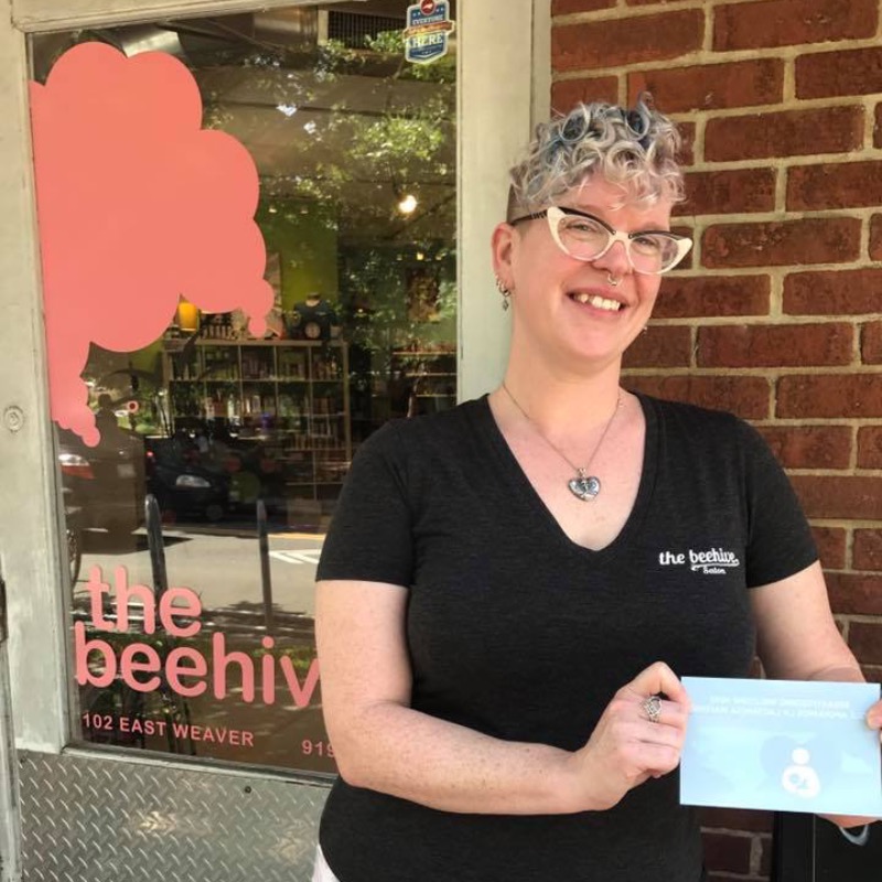 Employee in front of The Beehive door holding a breastfeeding communities cling