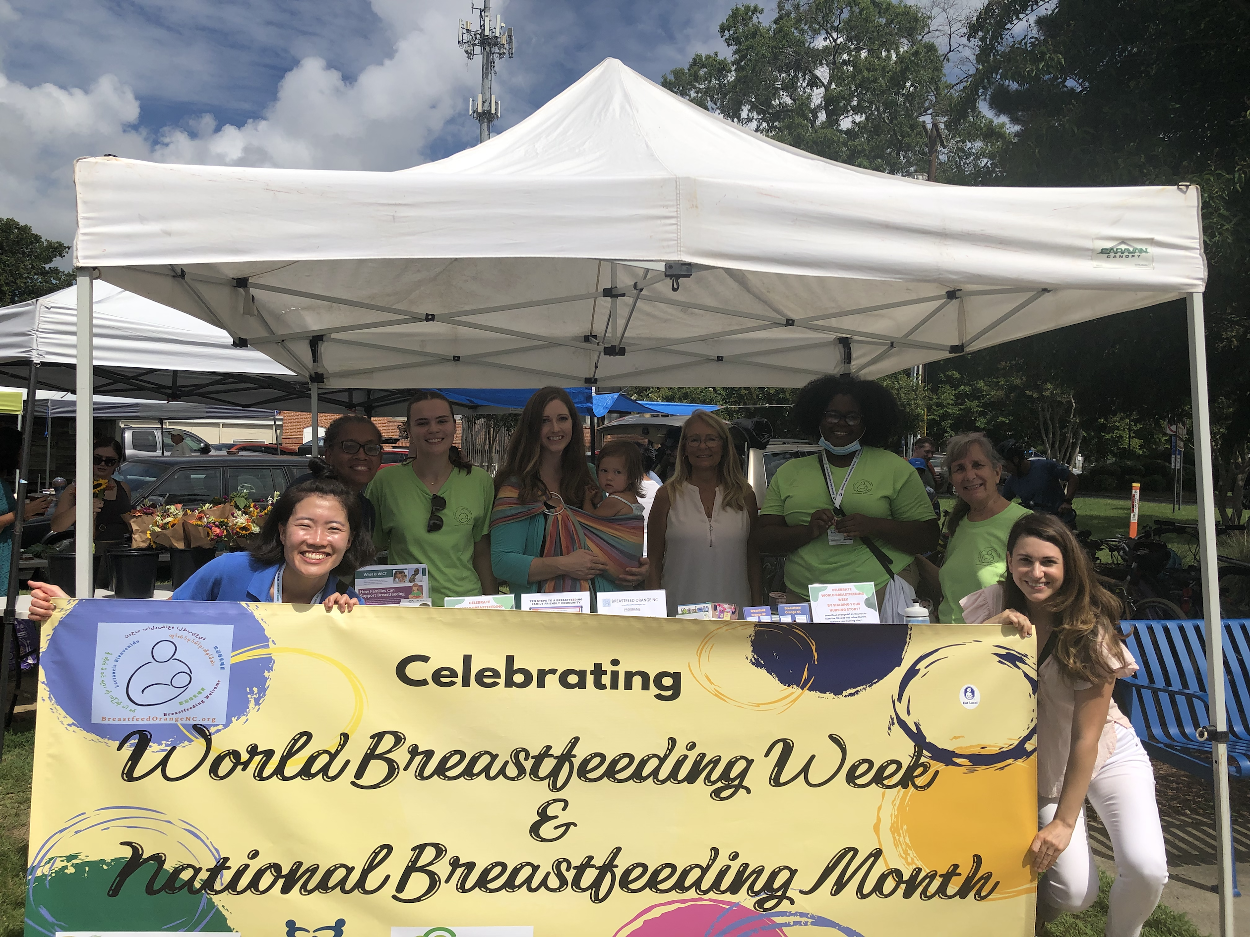 Eight adults and one child behind banner with text: Celebrating World Breastfeeding Week & National Breastfeeding Month.